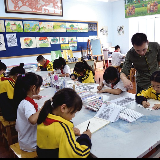 中国小学美术教室中，学生作品陈列在墙面上，孩子们正在专注创作
