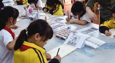 中国小学美术课桌上摆放着画笔、画册和正在使用的创作材料
